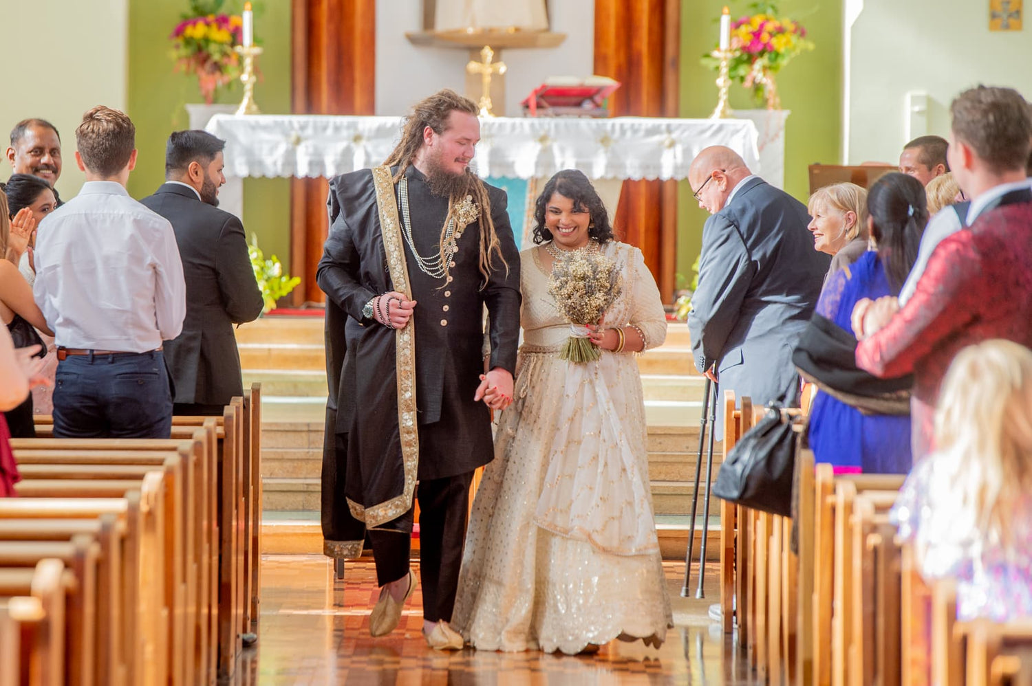 Wedding ceremony in a church with a couple walking down the aisle wearing a sherwani and lehenga for their fusion wedding