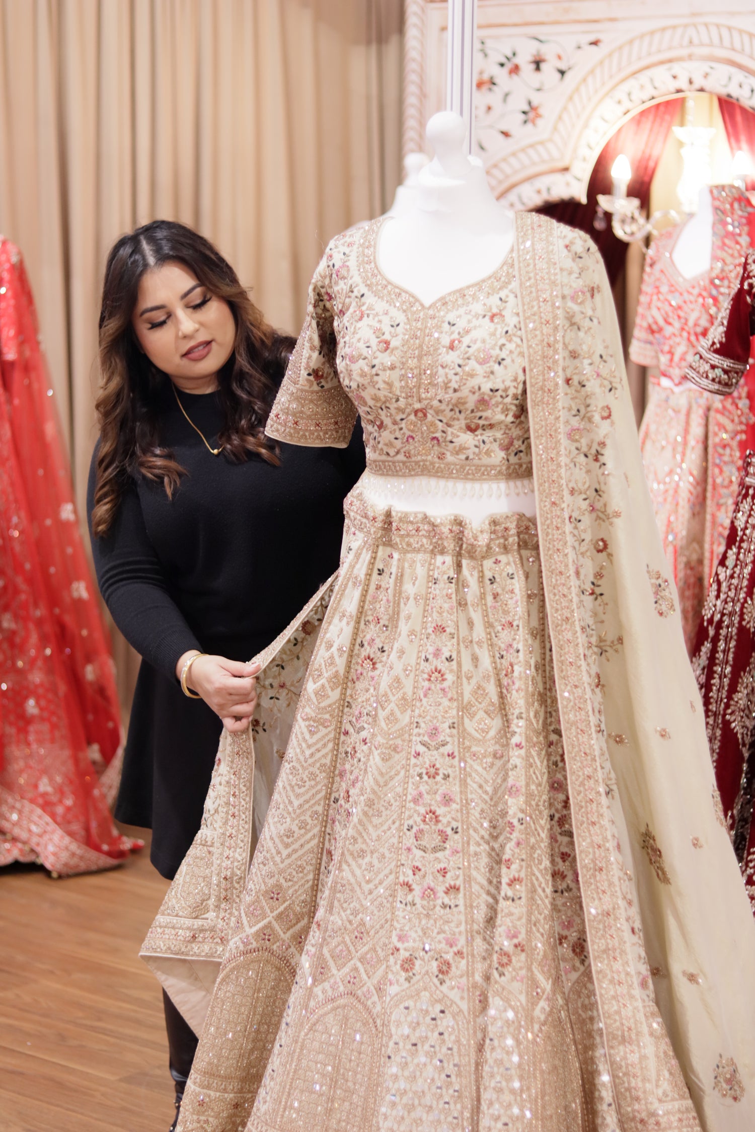 Trish Sherni London adjusting dupatta on a floral multi coloured Indian bridal lehenga on a white mannequin with mannequins around her