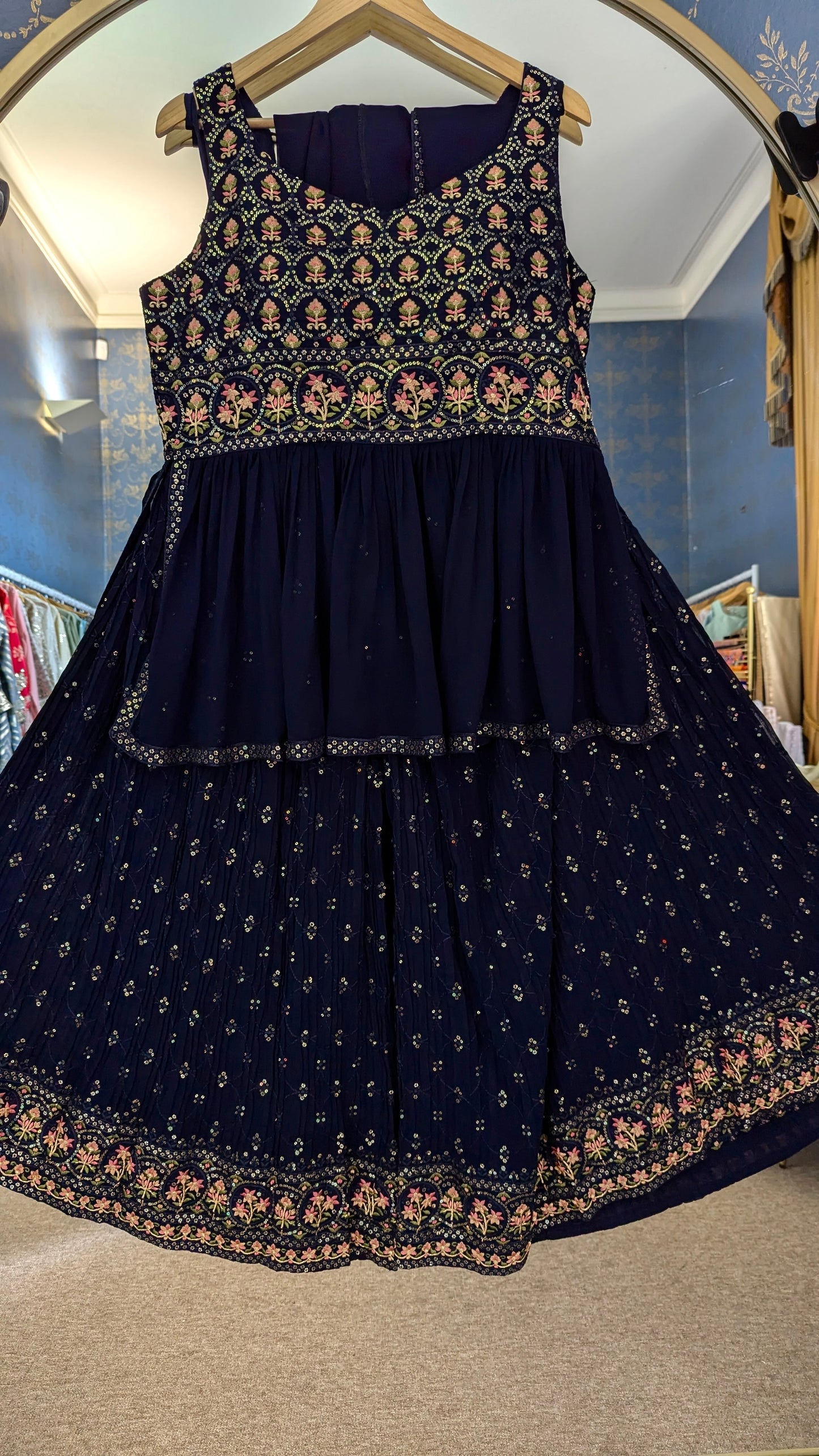 Navy blue peplum sharara with gold and threadwork floral embroidery on a hanger against a mirror background