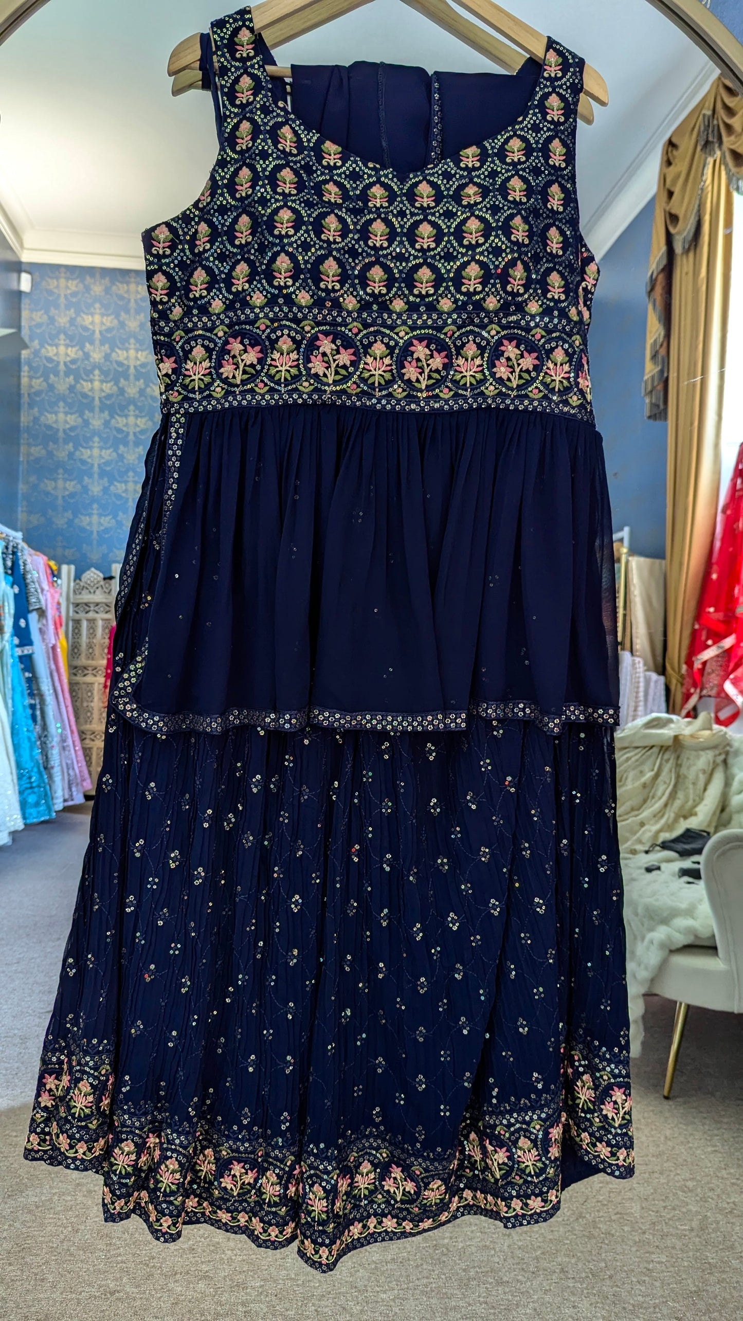 Navy blue peplum sharara with gold and threadwork floral embroidery on a hanger against a mirror background