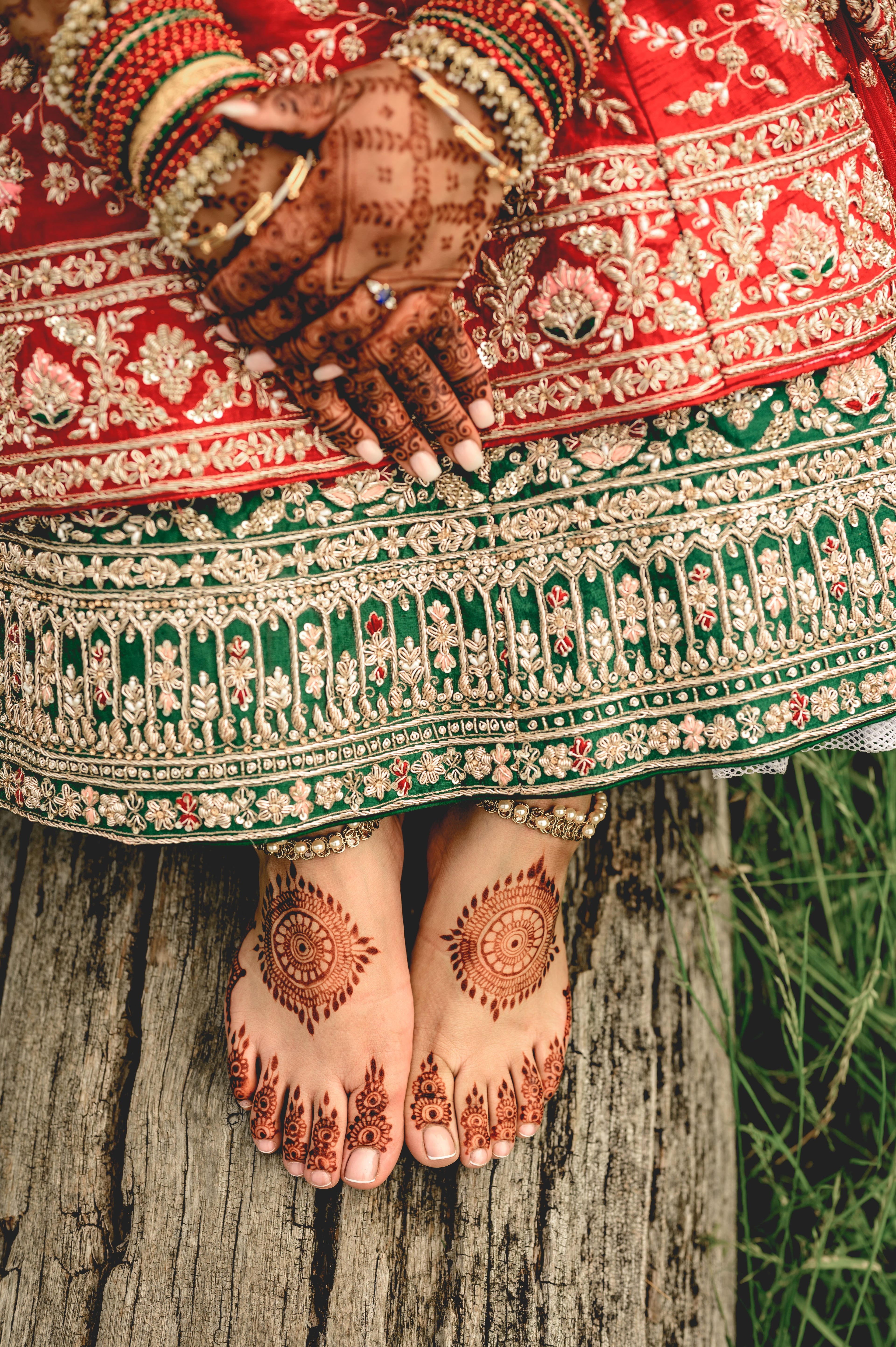 Sherni London Indian bride wearing a traditional embroidered red and gold lehenga with intricate henna designs on hands and feet.