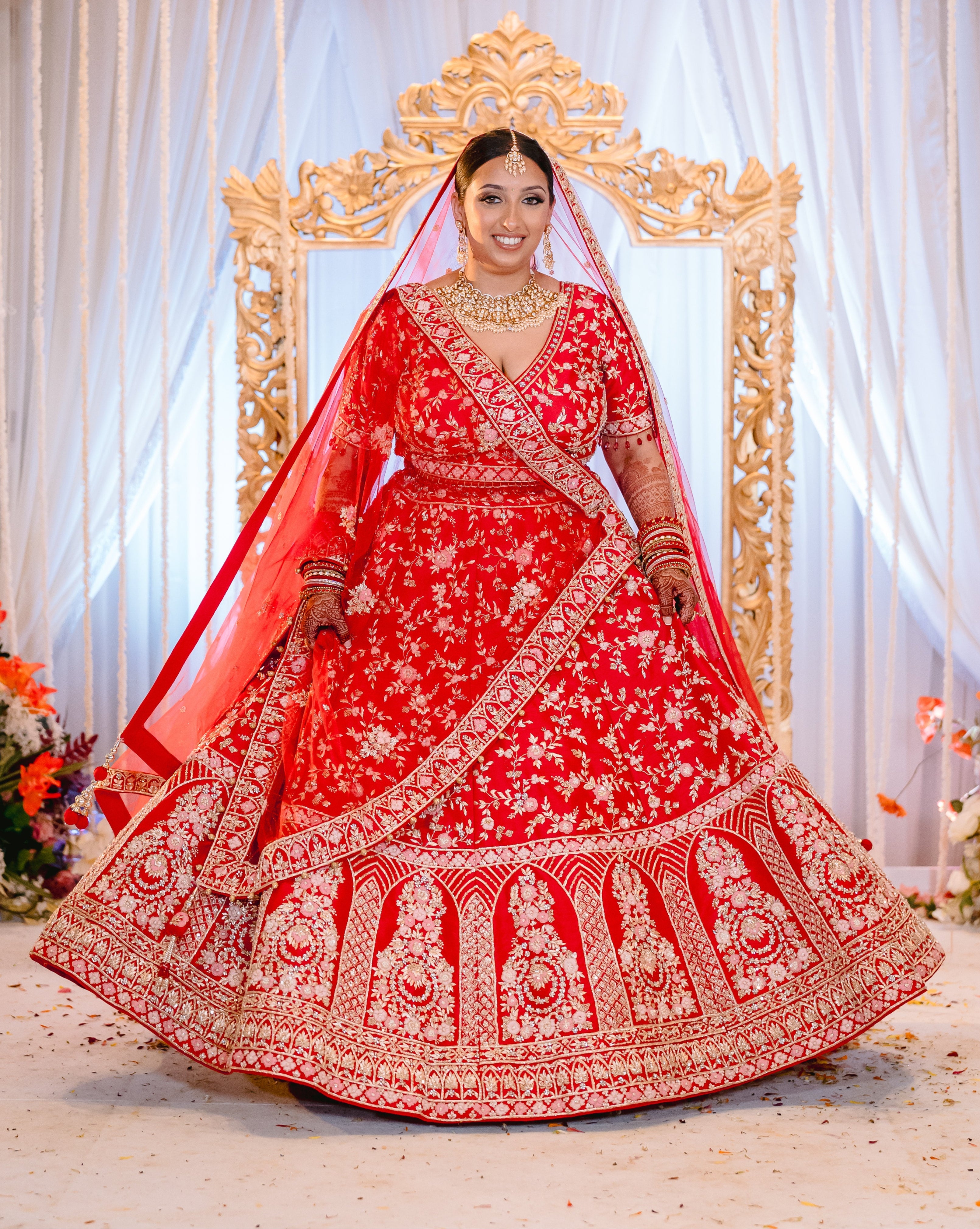 Sherni London Indian bride in red bridal lehenga with gold embroidery and two dupattas twirling at Hindu mandap ceremony