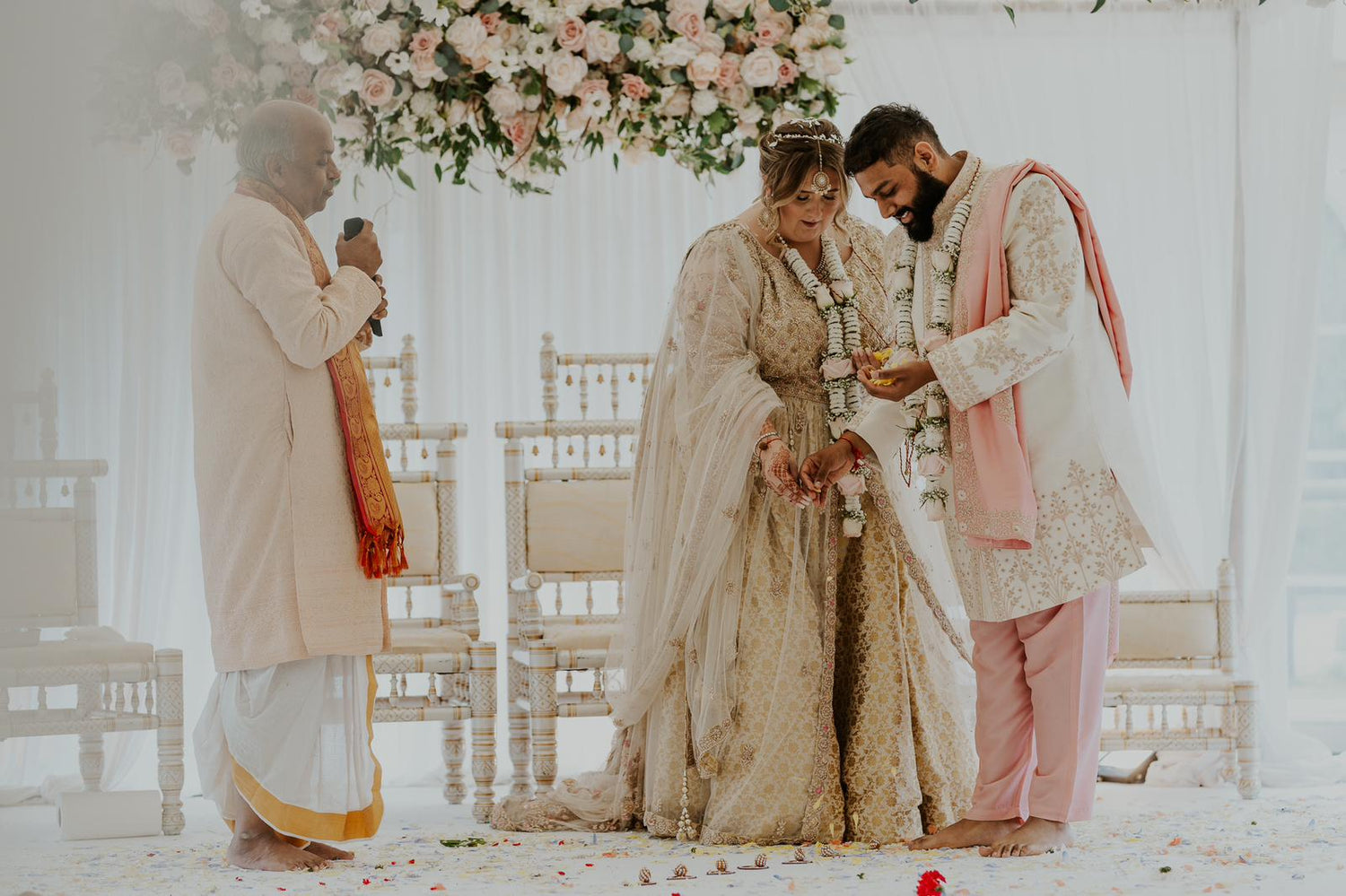 Fusion bride and groom in cream lehenga and cream and pink sherwani at Hindu wedding ceremony with priest