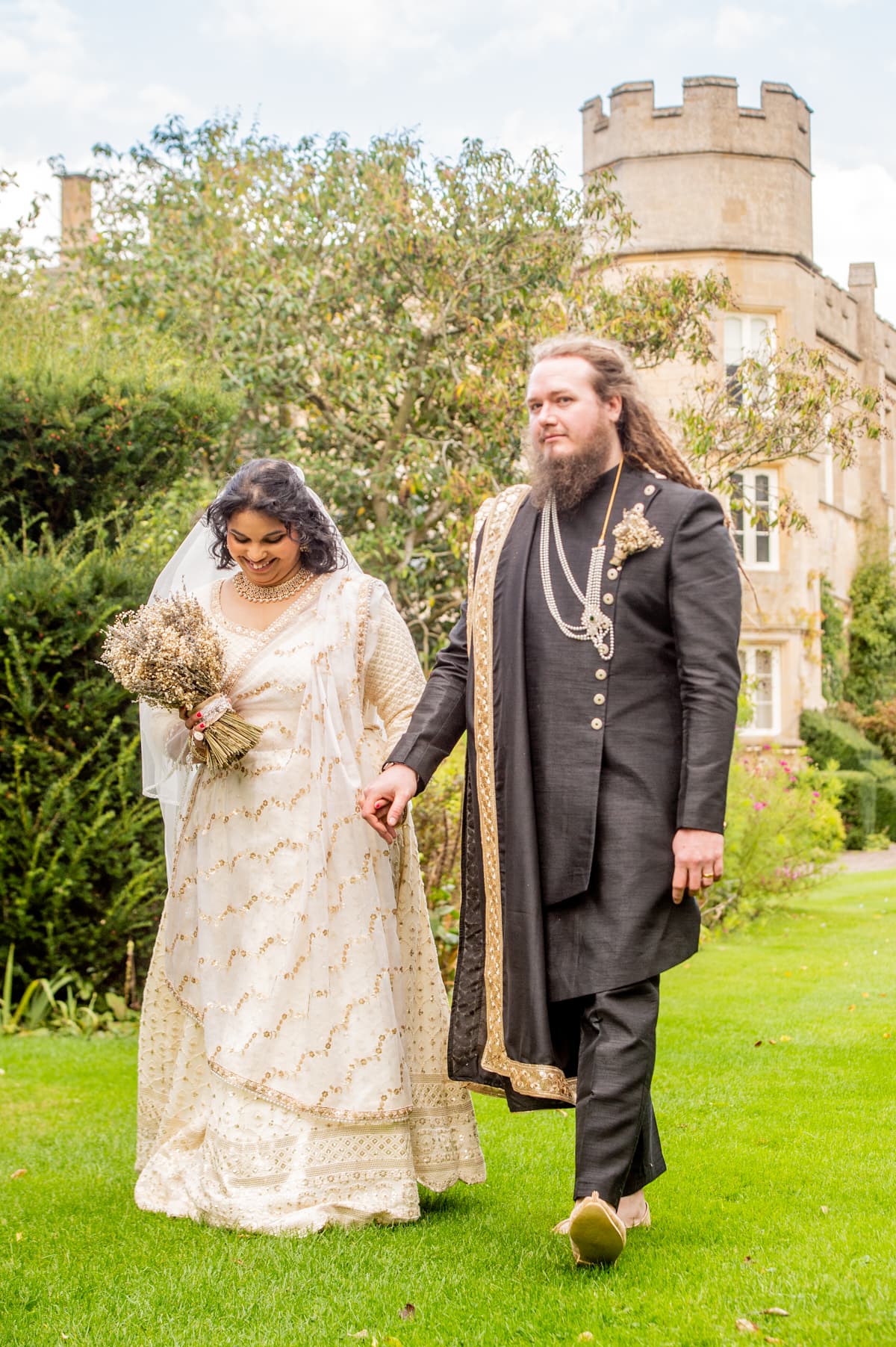 Sherni London bride and groom in fusion church wedding ceremony wearing white chikankari lucknowi lehenga and black asymmetric sherwani with gold buttons and trim