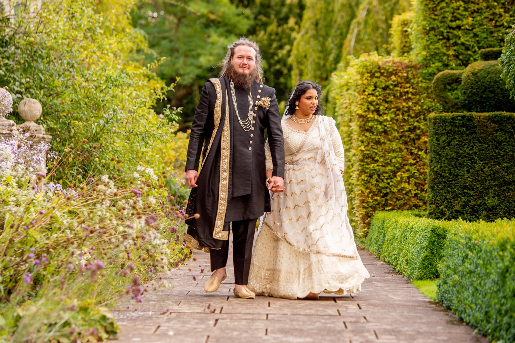 Sherni London bride and groom in fusion church wedding ceremony wearing white chikankari lucknowi lehenga and black asymmetric sherwani with gold buttons and trim