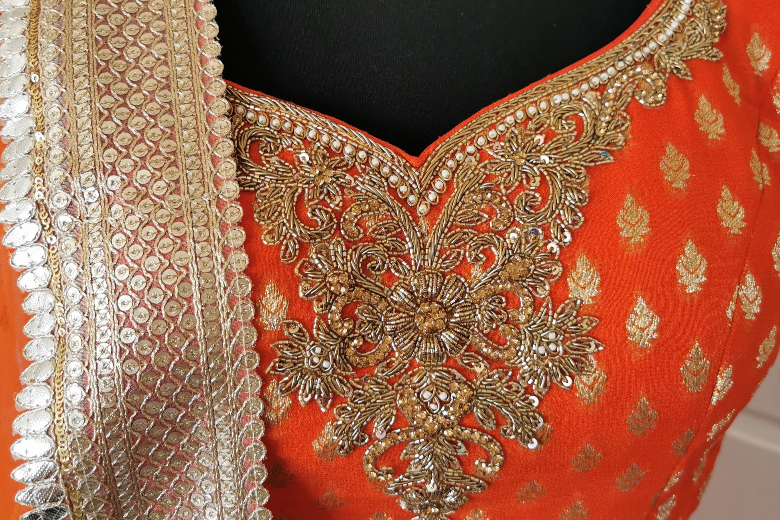 Sherni London orange lehenga choli blouse with gold embroidery on a mannequin against a white background