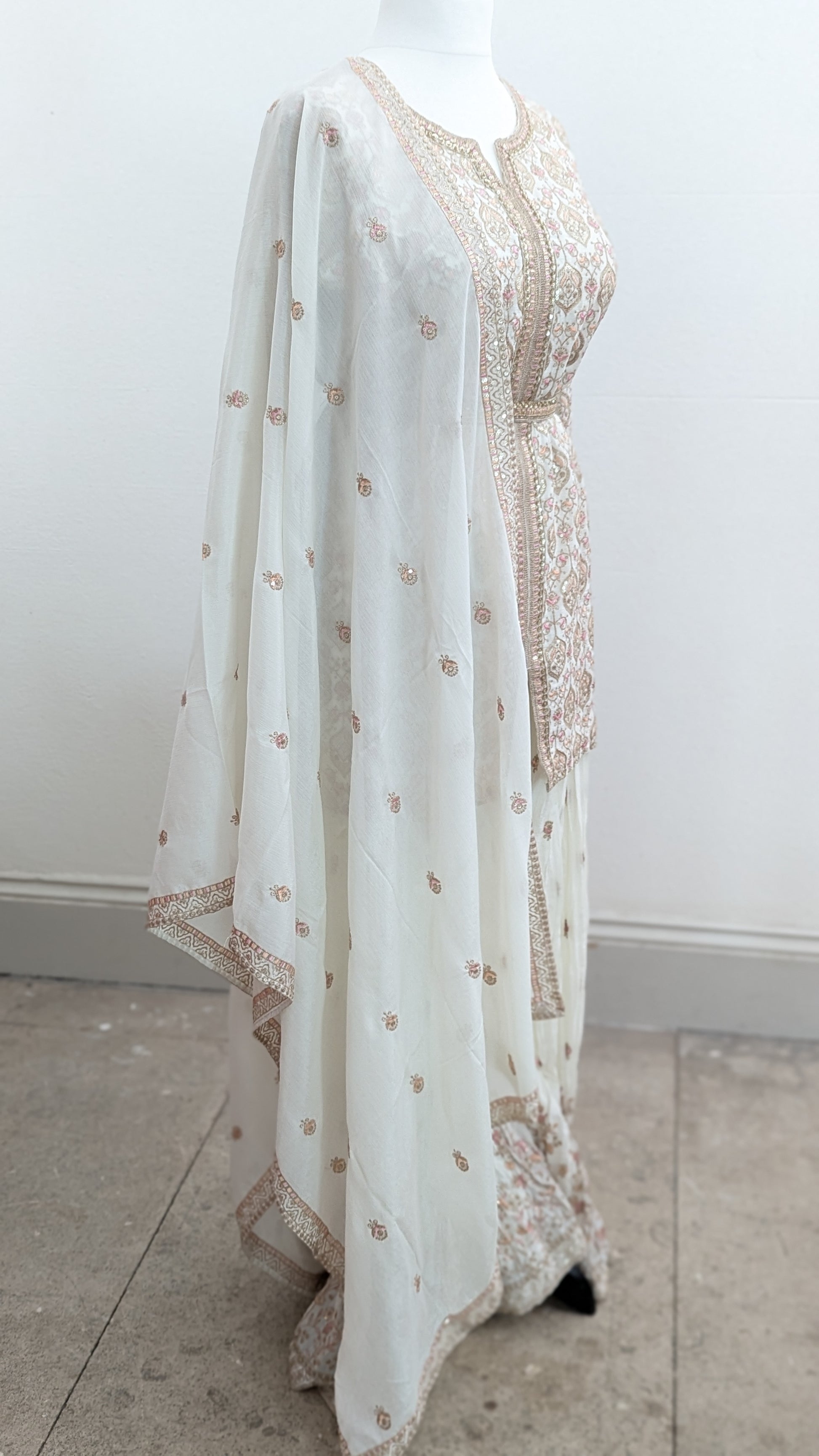Mannequin wearing a cream jacket sharara suit set with sequins hand embroidery and threadwork long sleeves belt and dupatta