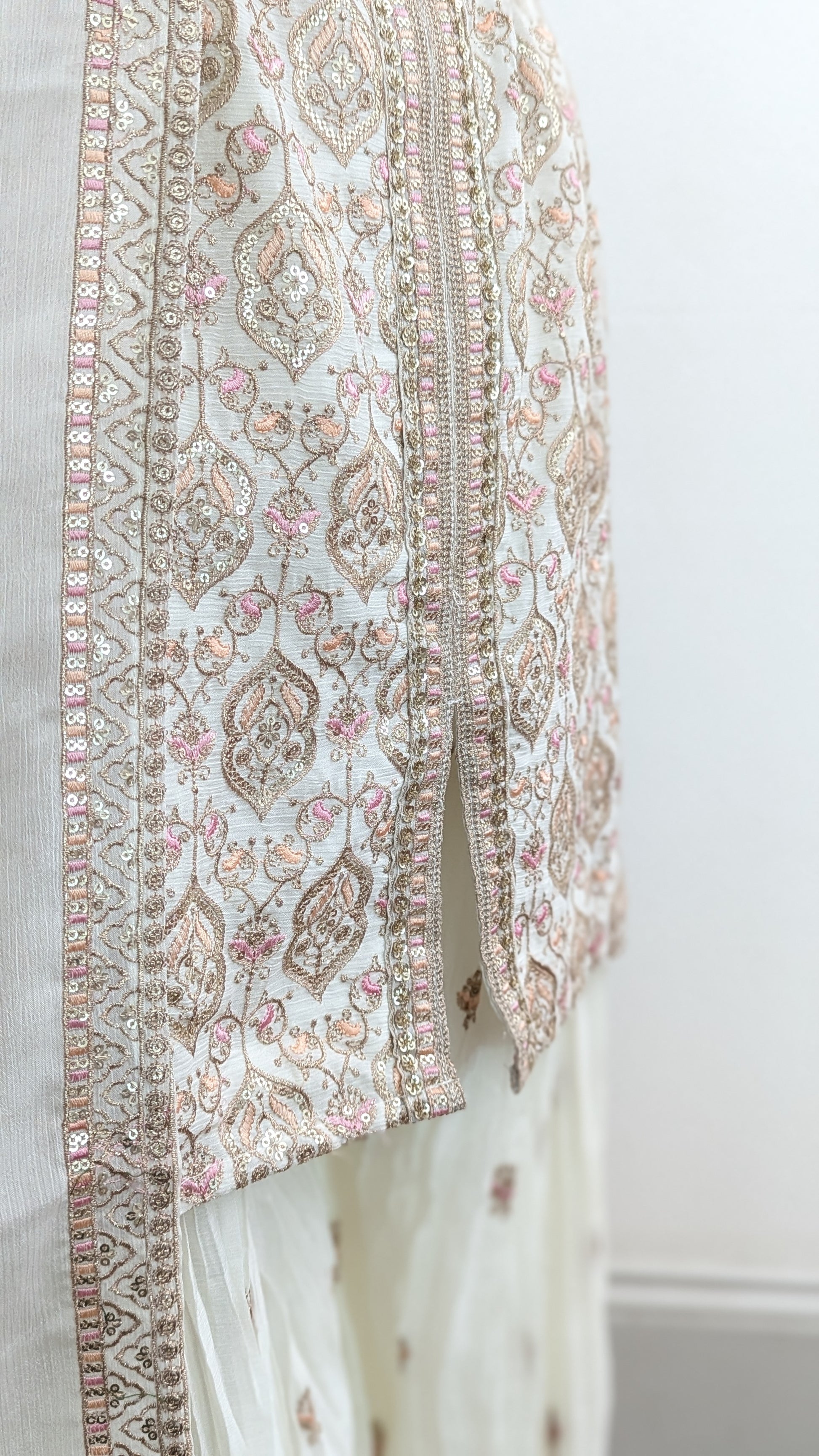 Mannequin wearing a cream jacket sharara suit set with sequins hand embroidery and threadwork long sleeves belt and dupatta