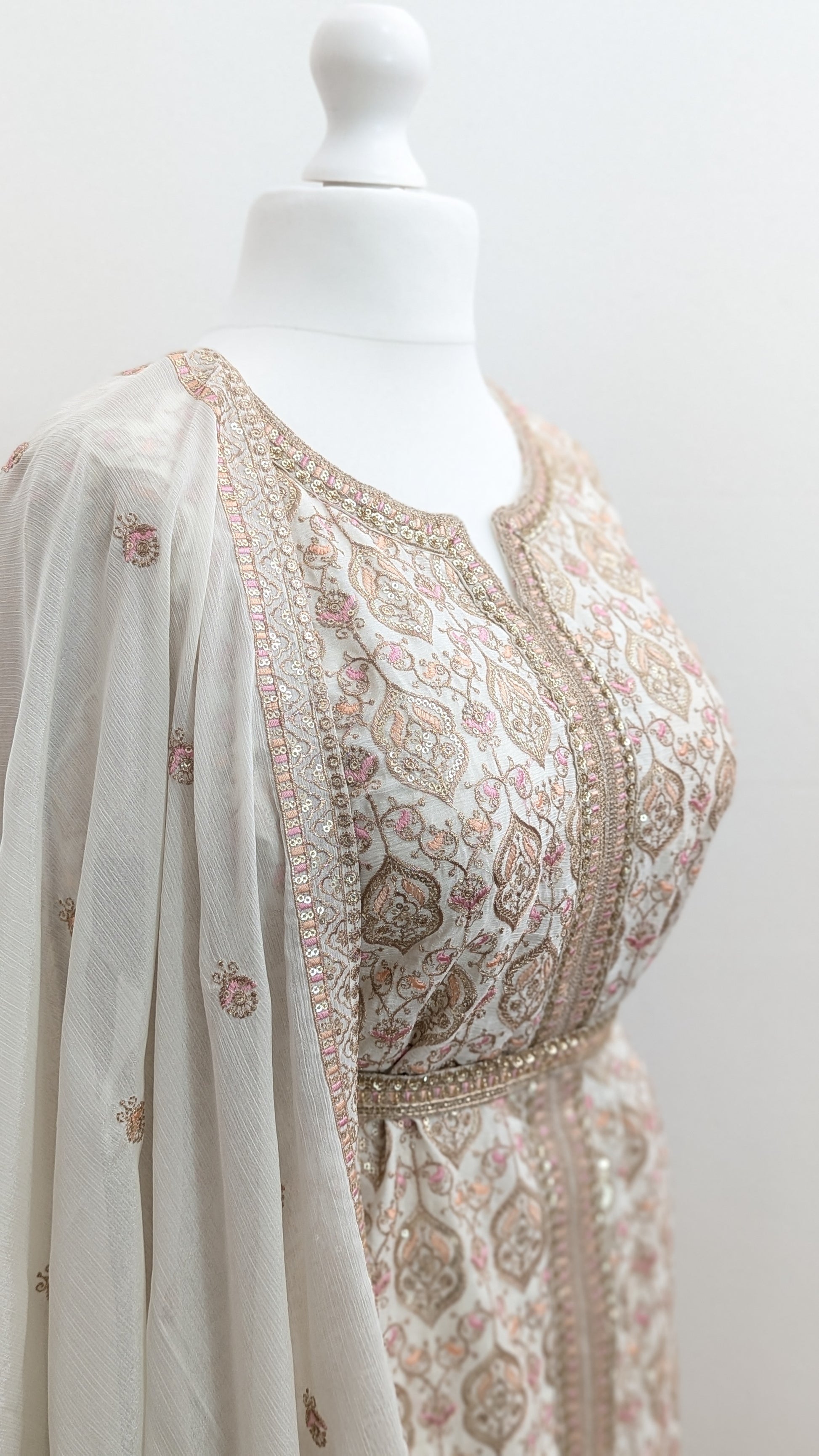 Mannequin wearing a cream jacket sharara suit set with sequins hand embroidery and threadwork long sleeves belt and dupatta