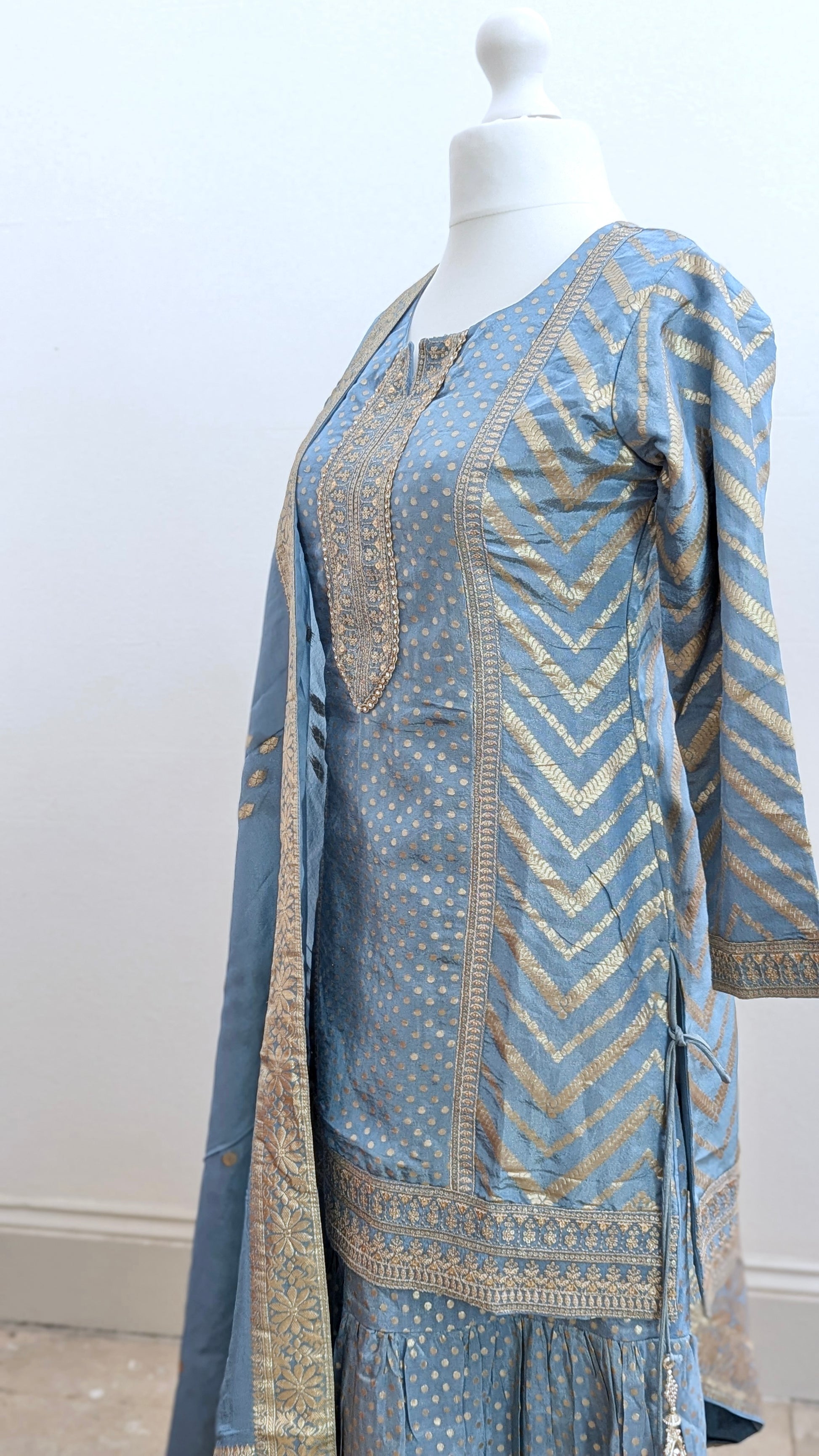 Mannequin with traditional gharara suit in blue grey with gold benarsi print and chevron design all over with sleeves and side tassels