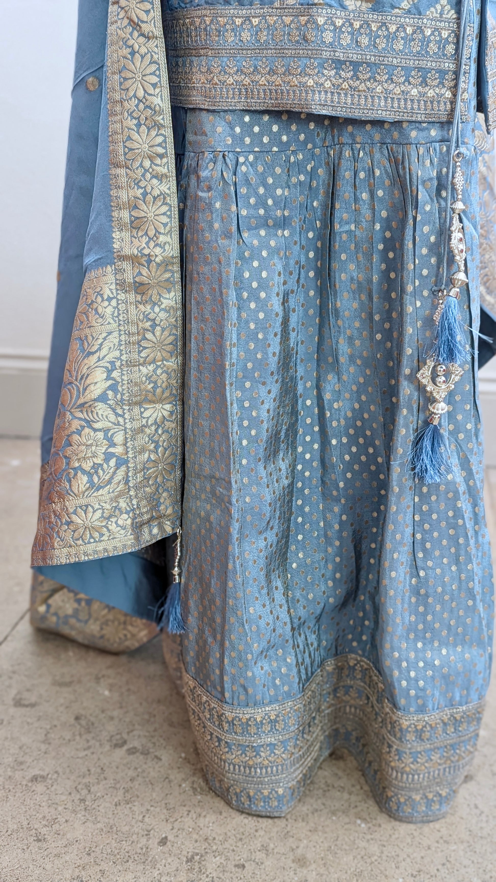 Mannequin with traditional gharara suit in blue grey with gold benarsi print and chevron design all over with sleeves and side tassels
