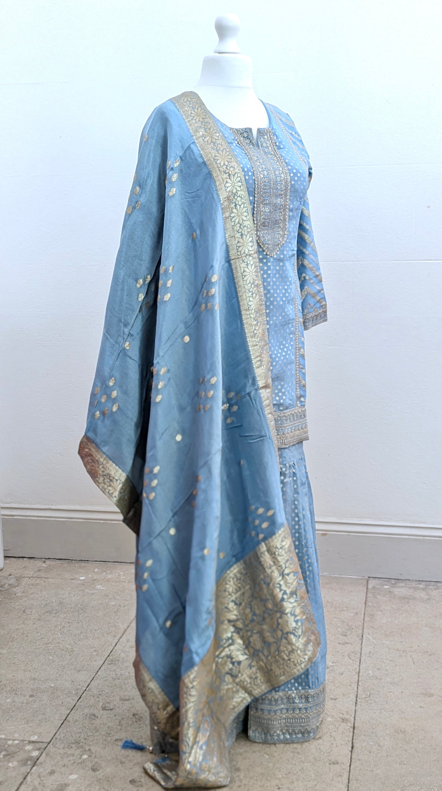 Mannequin with traditional gharara suit in blue grey with gold benarsi print and chevron design all over with sleeves and side tassels