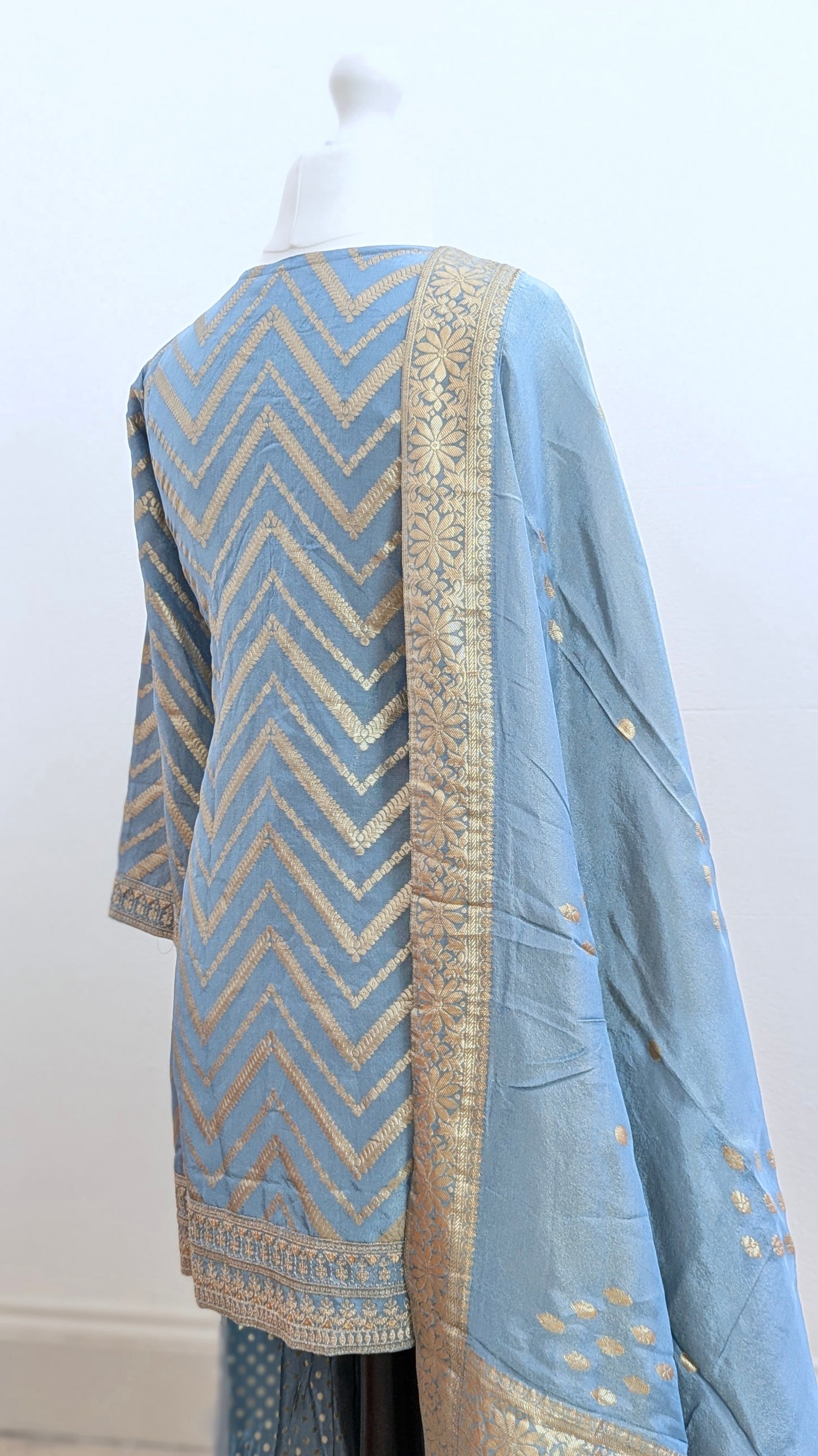 Mannequin with traditional gharara suit in blue grey with gold benarsi print and chevron design all over with sleeves and side tassels