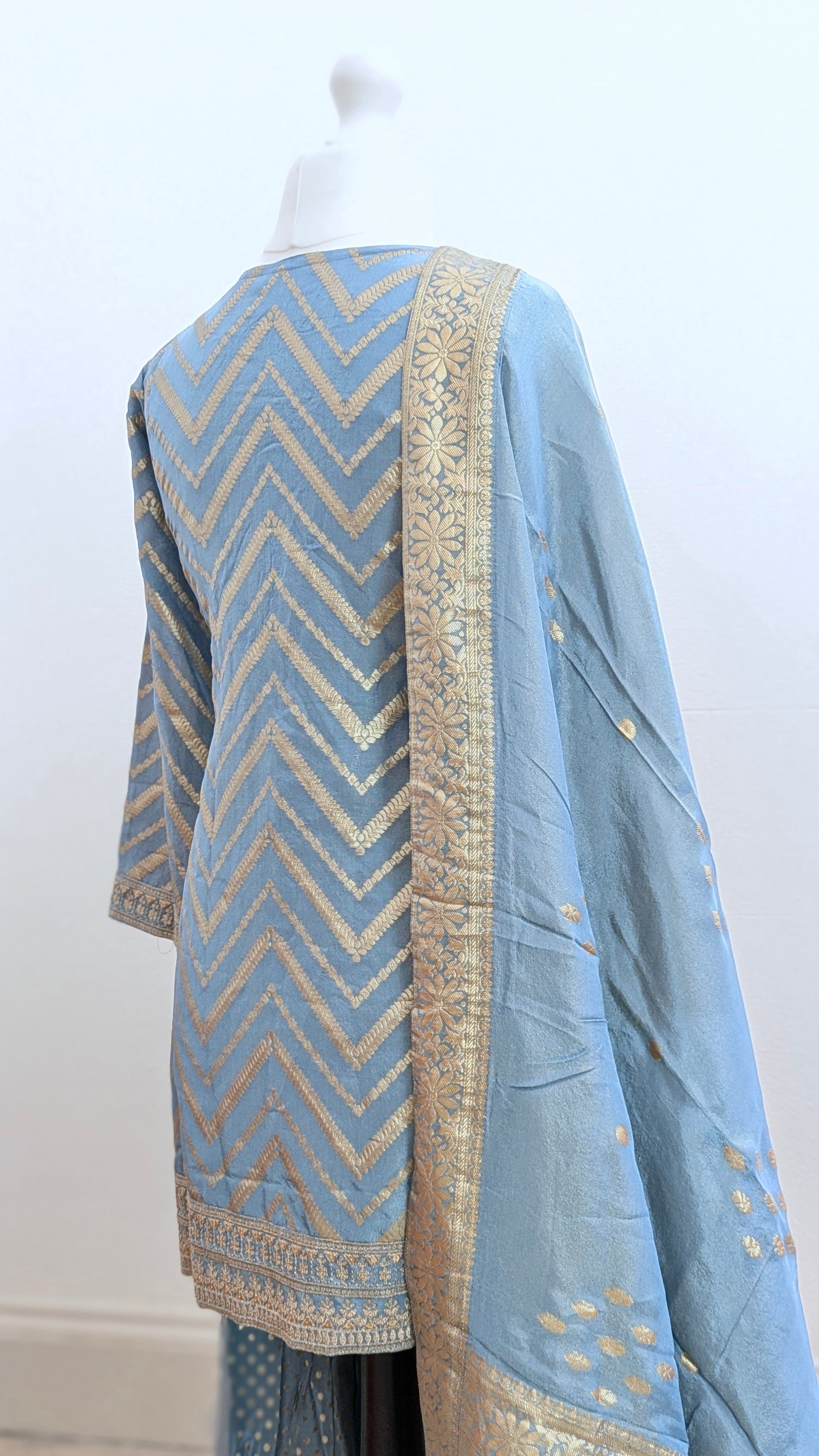 Mannequin with traditional gharara suit in blue grey with gold benarsi print and chevron design all over with sleeves and side tassels