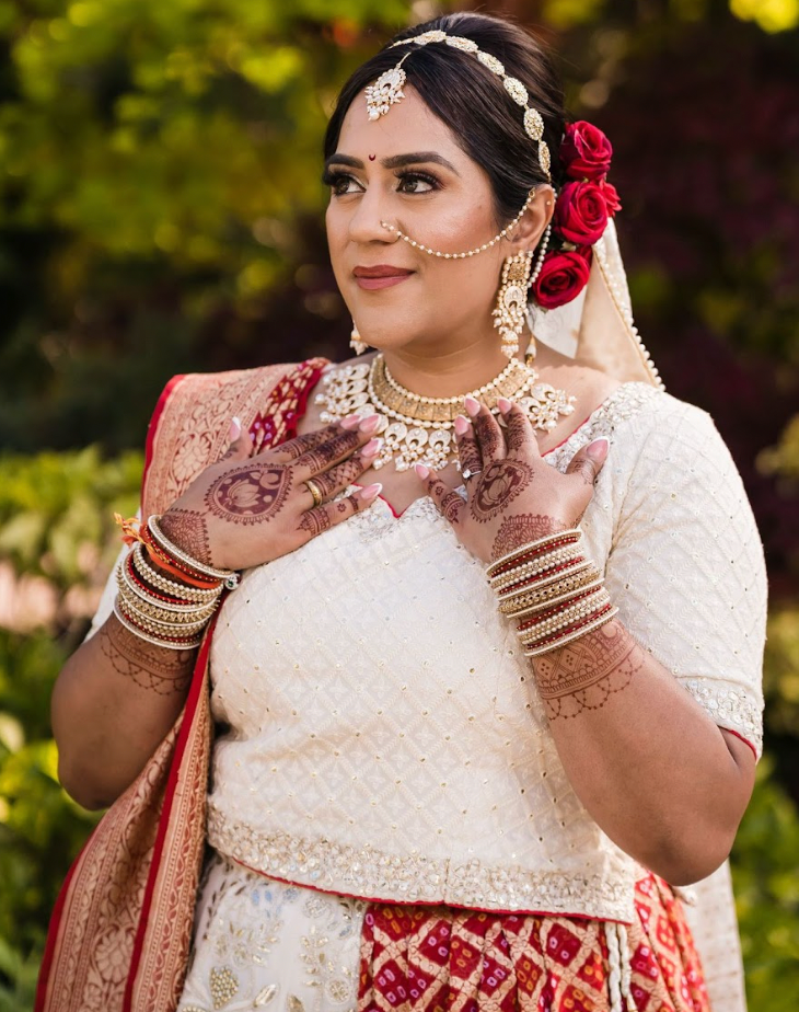 Sherni London Indian bride in cream chikankari lucknowi lehenga with gold hand embroidery henna on hands and red saree draped around and red flowers in hair