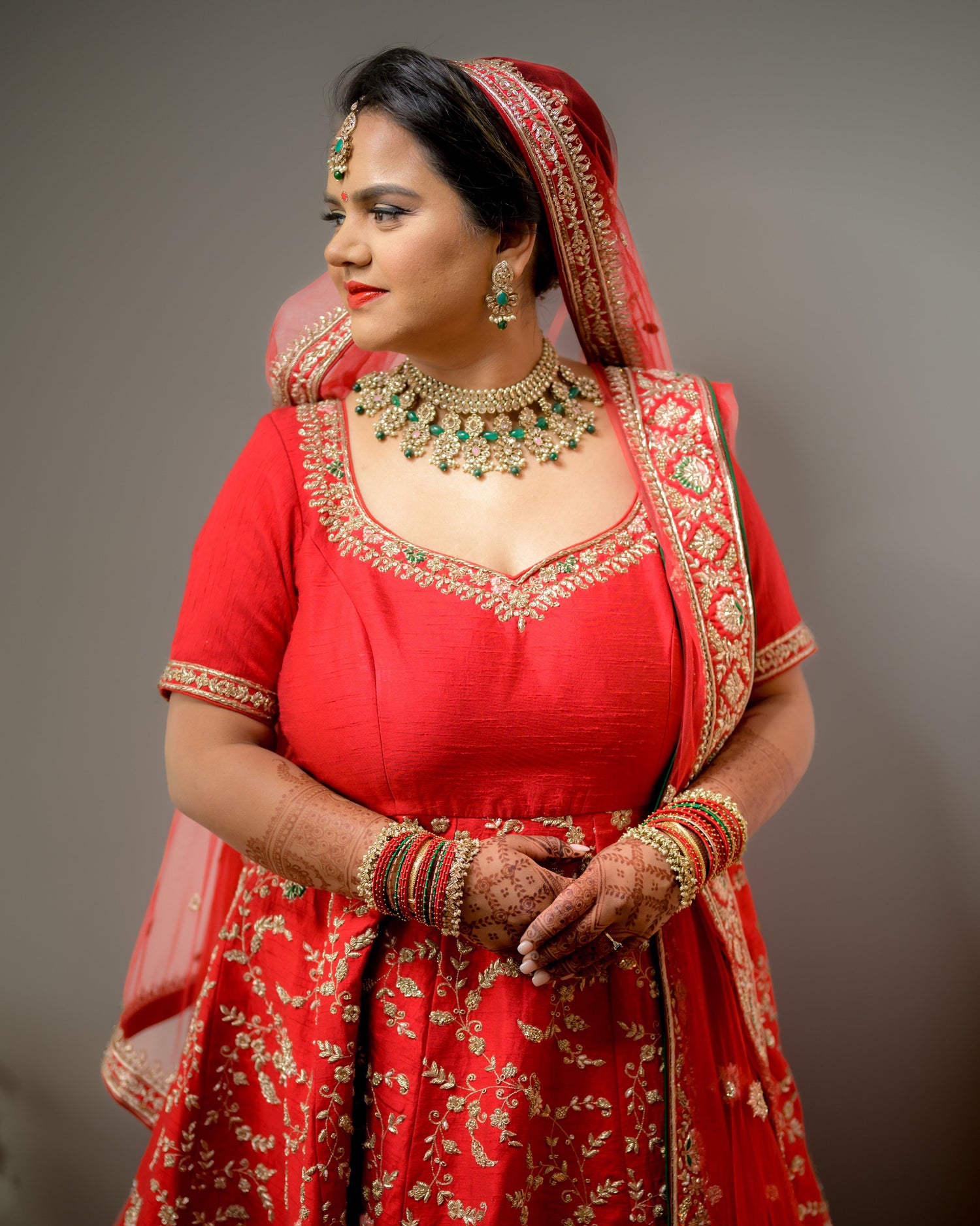 Woman in a traditional red outfit with gold embroidery and jewelry against a gray background