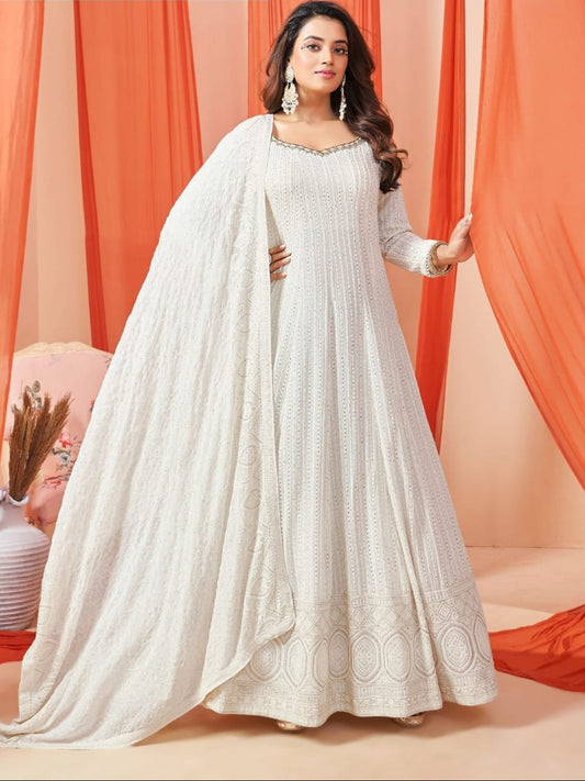 Woman wearing a white chikankari lucknowi dress with a matching dupatta against an orange curtain background.